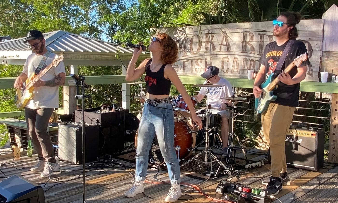The four member group, The Band Madam, performing on an outside stage on a sunny day