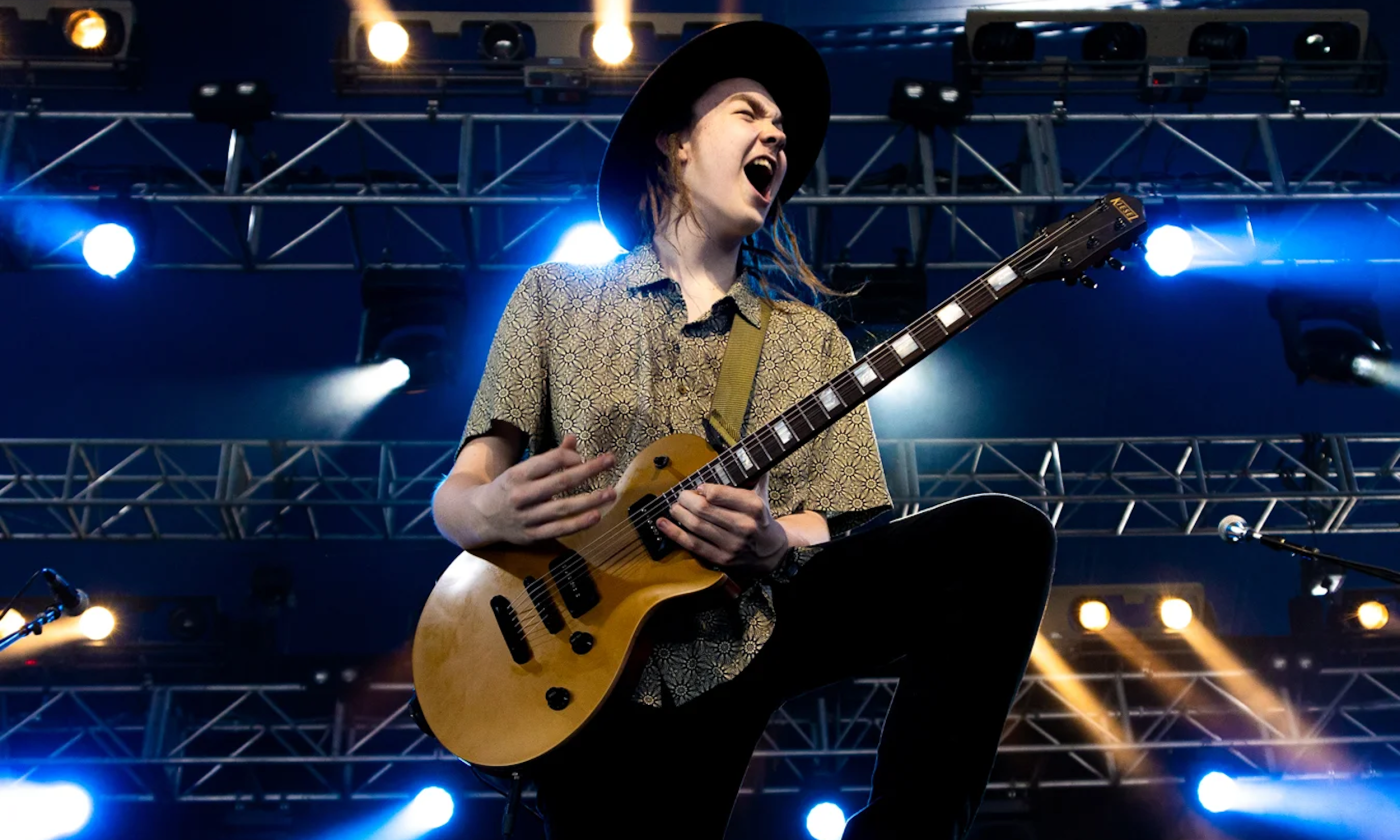 Taj Farrant plays his guitar beneath glowing blue and white stage lights.
