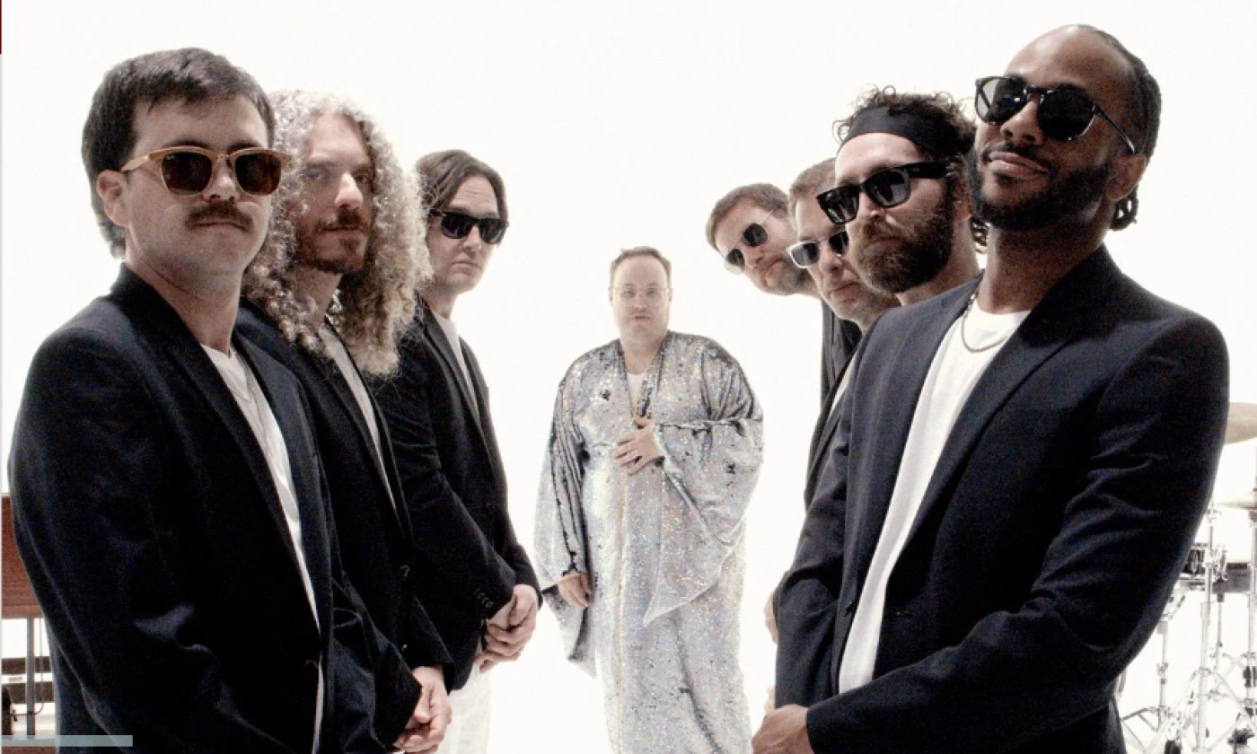 Bandmates from St. Paul & The Broken Bones wear dark clothing and pose in front of a white backdrop.