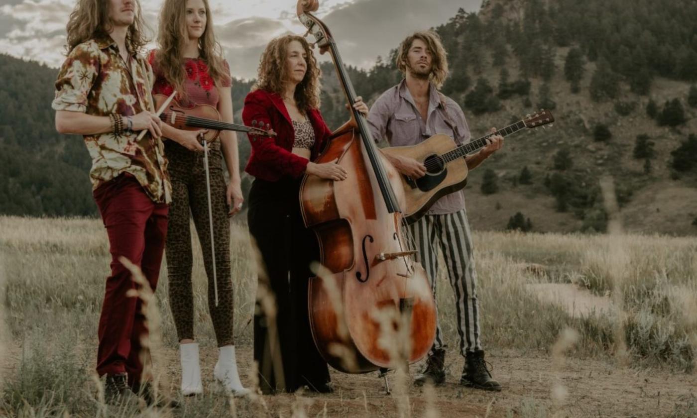 Bandmates from The Sweet Lilies stand with their instruments against a sweeping backdrop of trees and rolling hills.