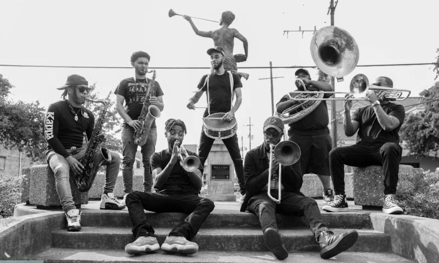 Trombone Shorty & Orleans Avenue and Juvenile sit on a staircase and pose with musical instruments.