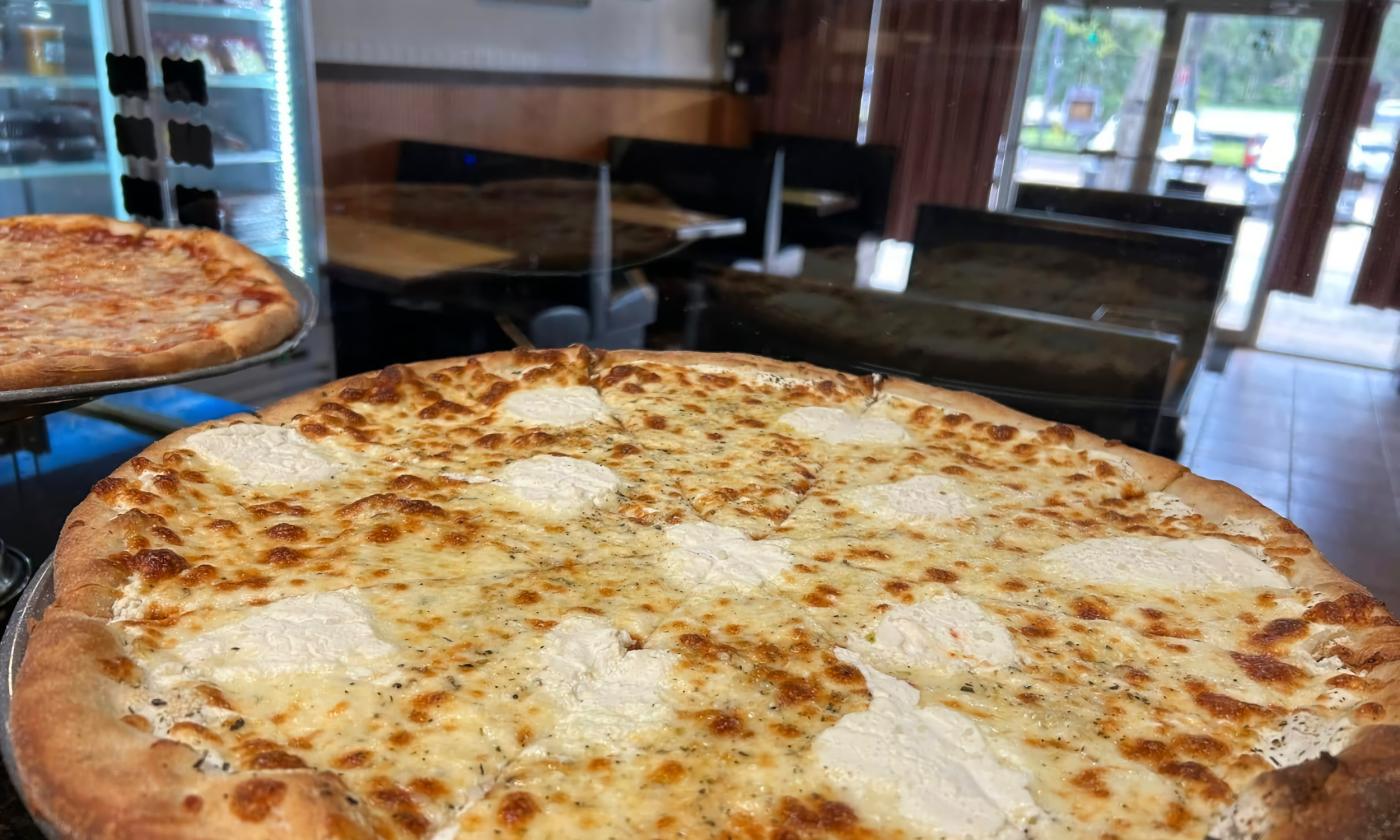 A large white pizza on a restaurant counter with booths and the door in the background