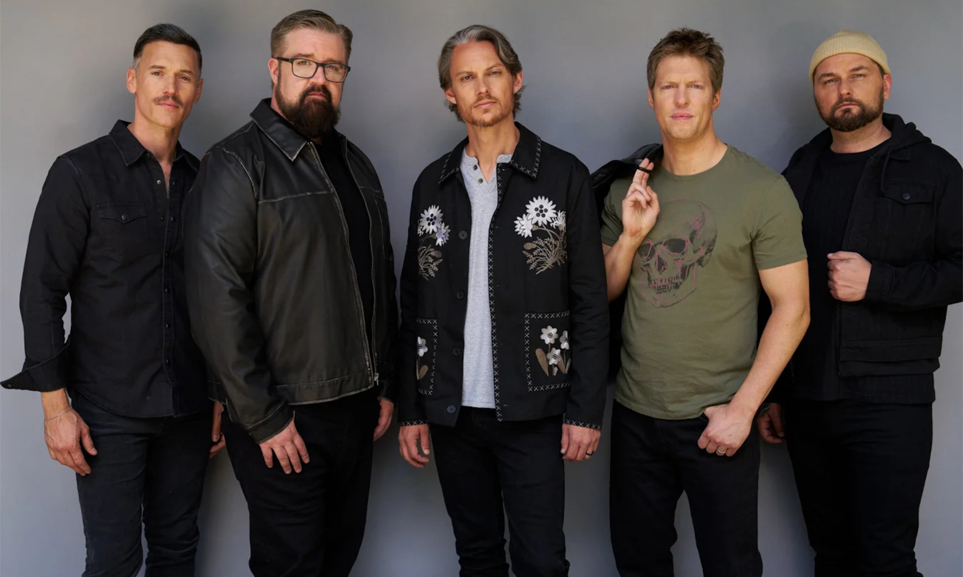 Bandmates from Home Free wear dark clothing and pose in front of a gray backdrop. 
