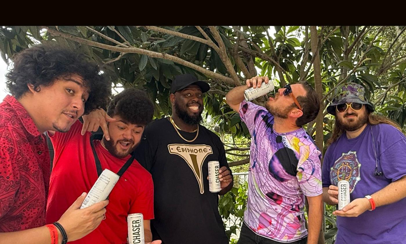 The band Tru Phonic vamping under tropical trees, with canned water, in the back of an SUV