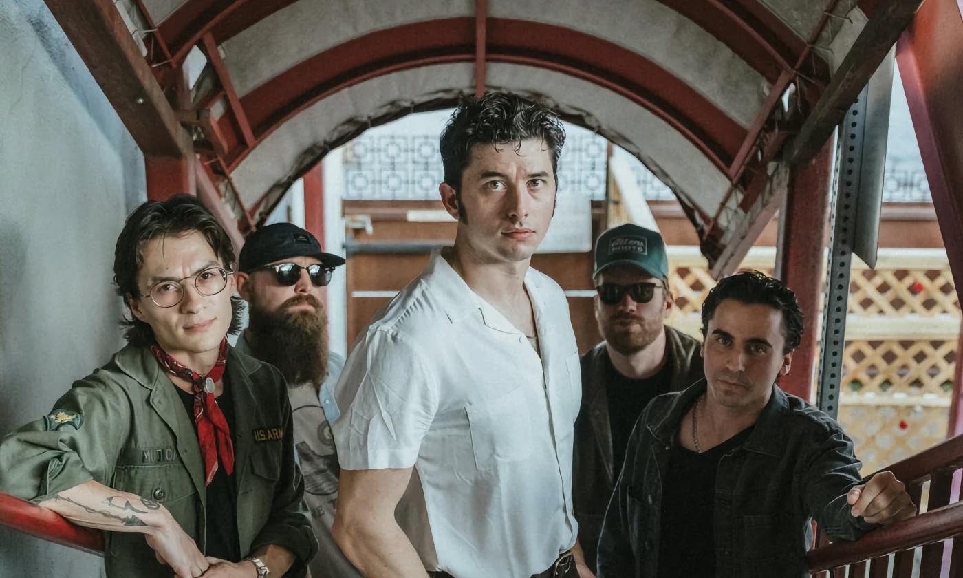 Nik Parr and the four members of The Selfless Lovers standing on an outdoor, Spanish-styled stairway