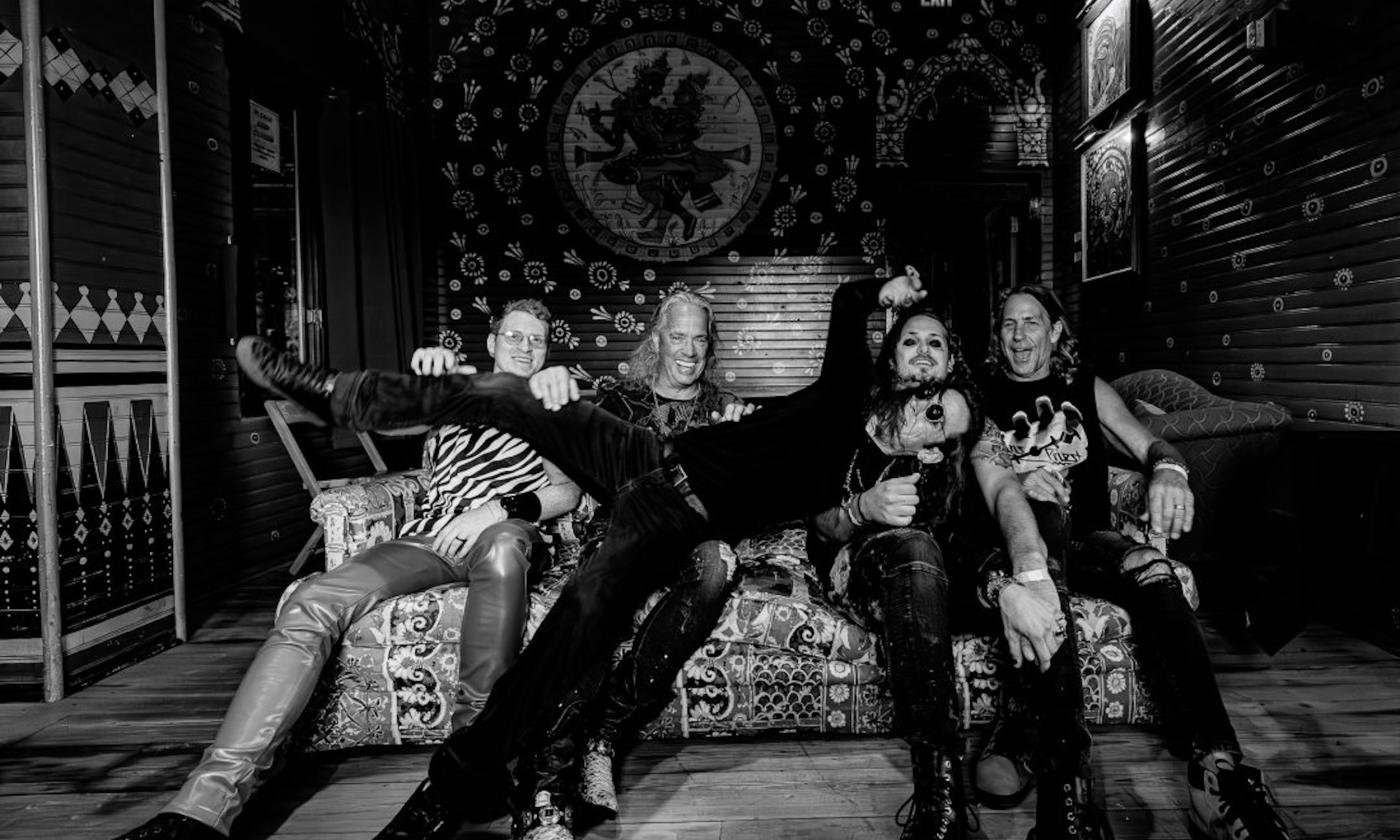 Bandmates from Flying High Again smile and pose on a couch.