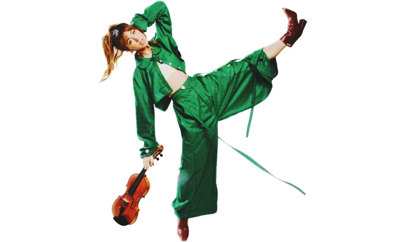 Lindsey Stirling wears a green outfit and poses with her violin.