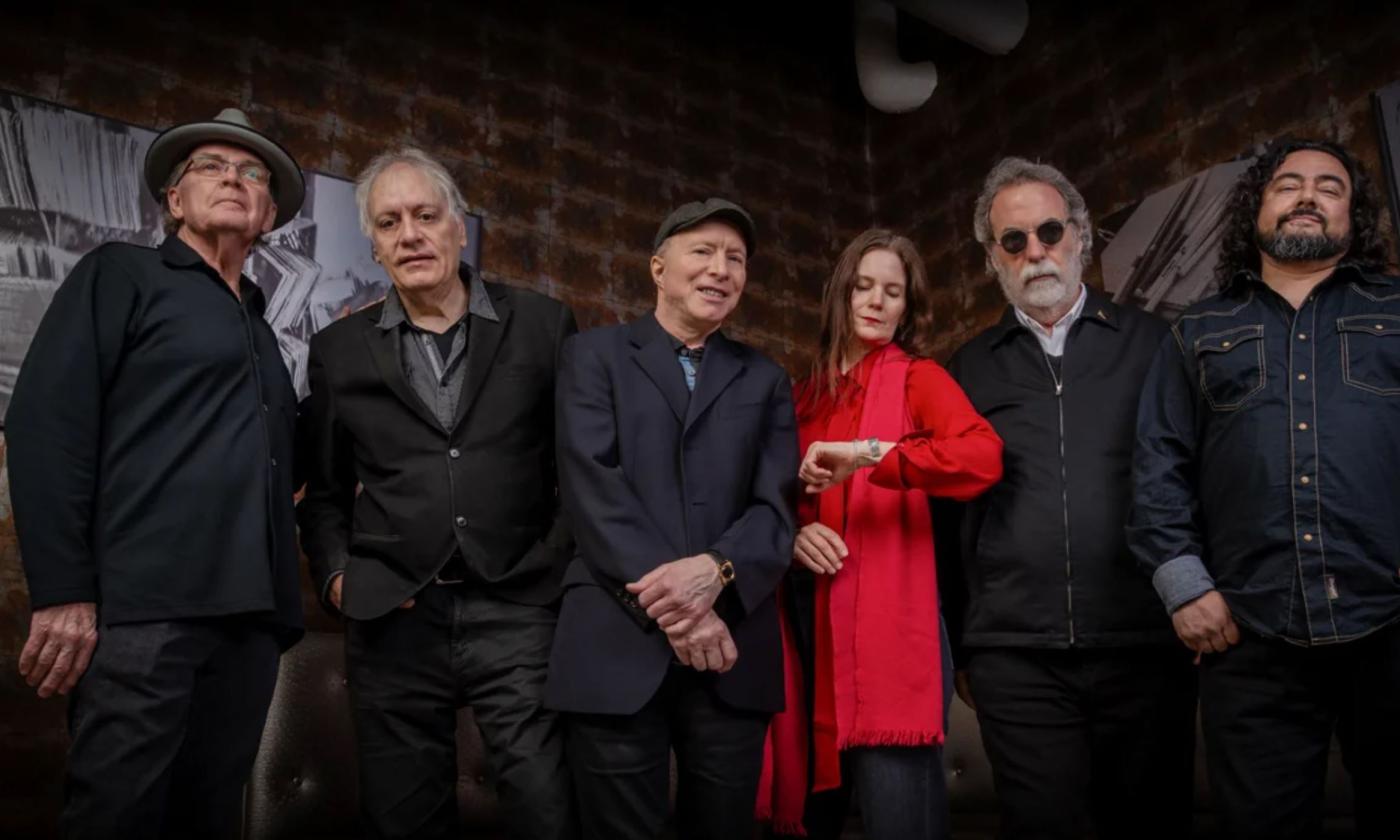 Bandmates from 10,000 Maniacs pose in front of a brick wall. 