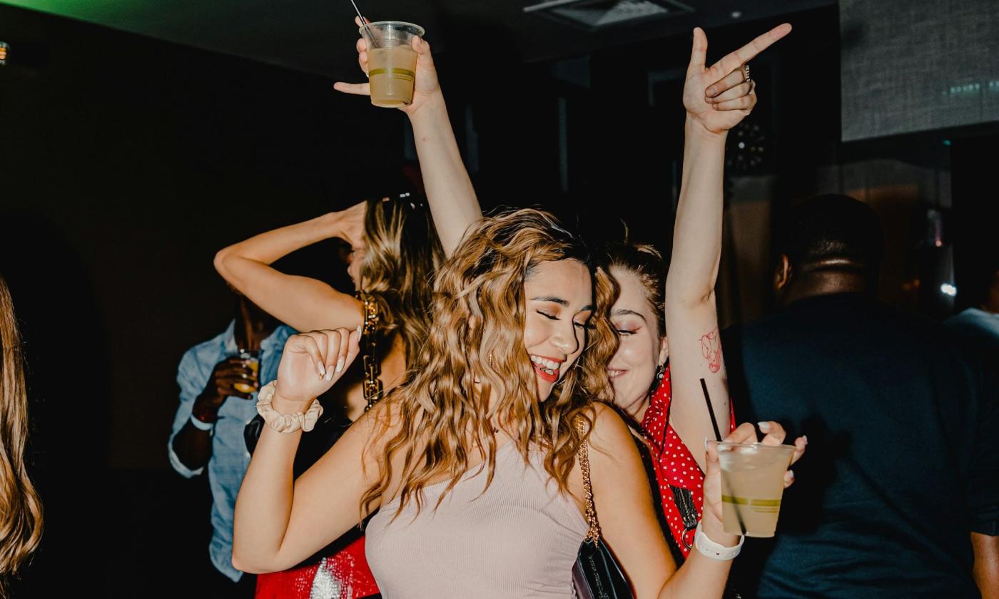 Two young women smile and dance at a party. 