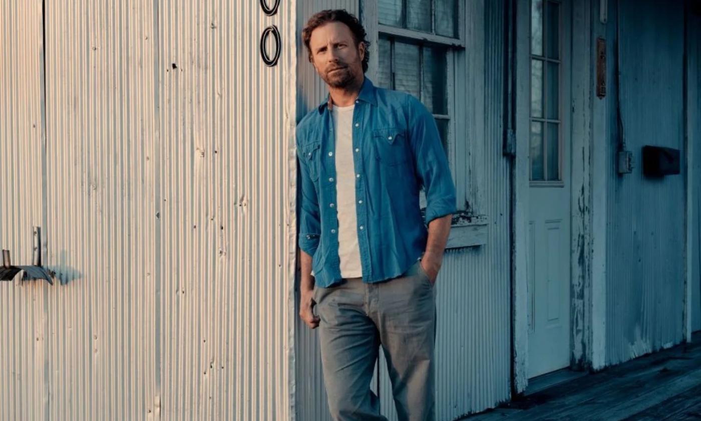Dierks Bentley wears a denim jacket and poses at the side of a building.