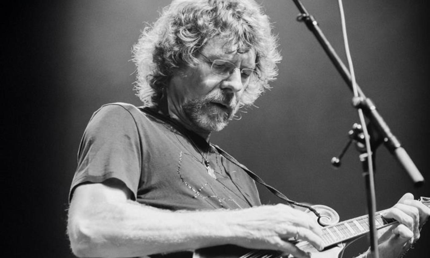 Sam Bush clutches his guitar and performs on stage. 