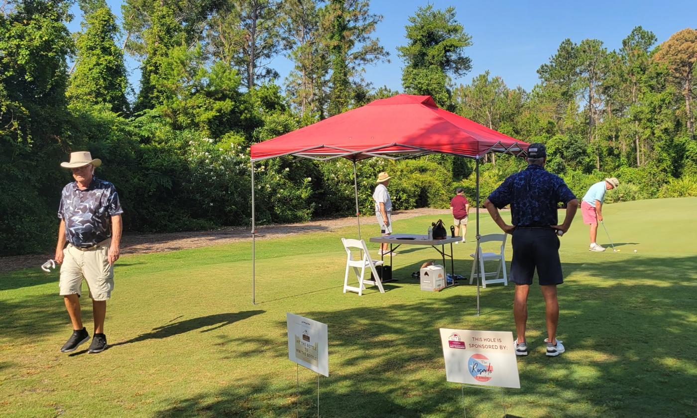 Signs, an awning, and players at the Catholic Chartites golf tournament in 2025