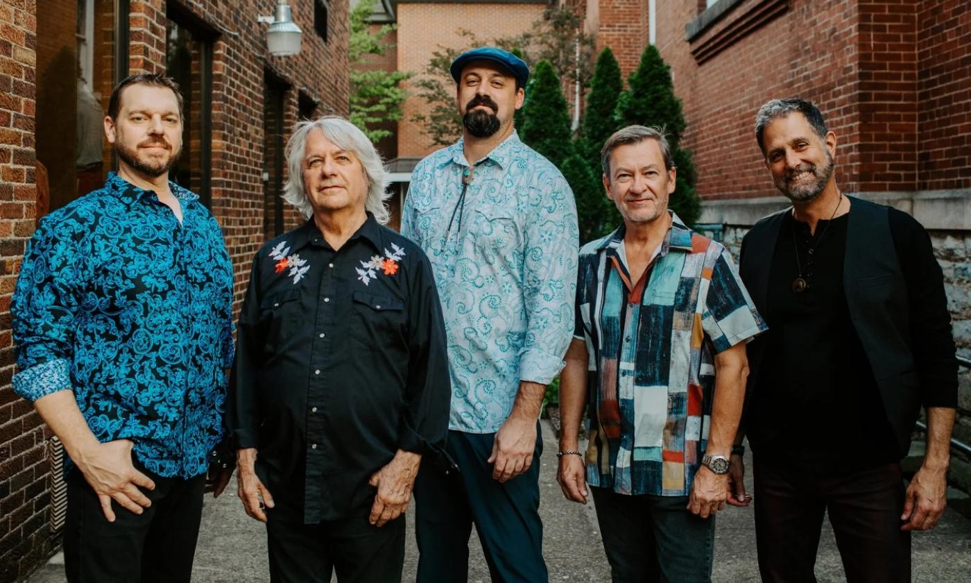 Bandmates from Pure Prairie League smile and pose in front of two brick buildings.