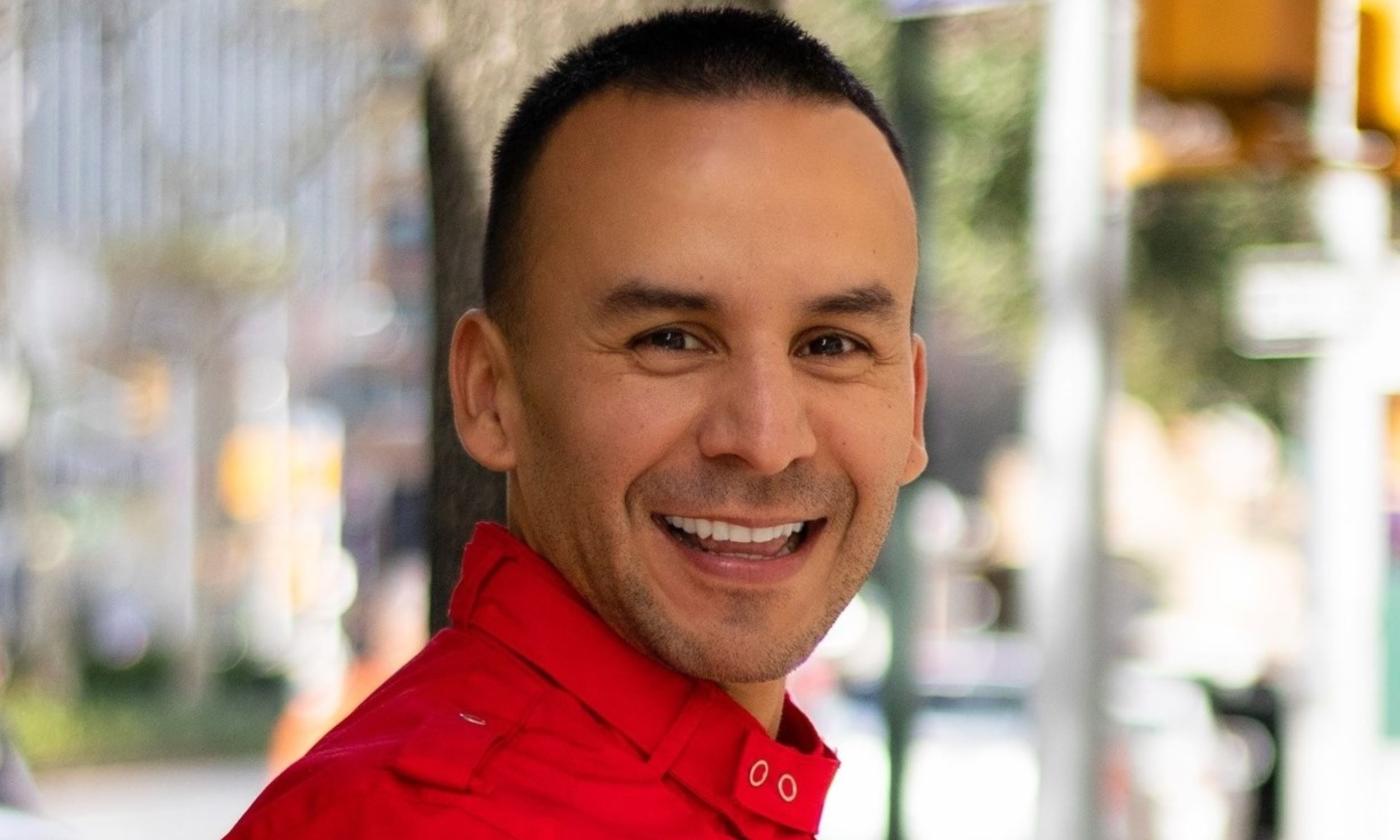 Pedro Gonzalez wears a red shirt and smiles in front of a blurred backdrop.