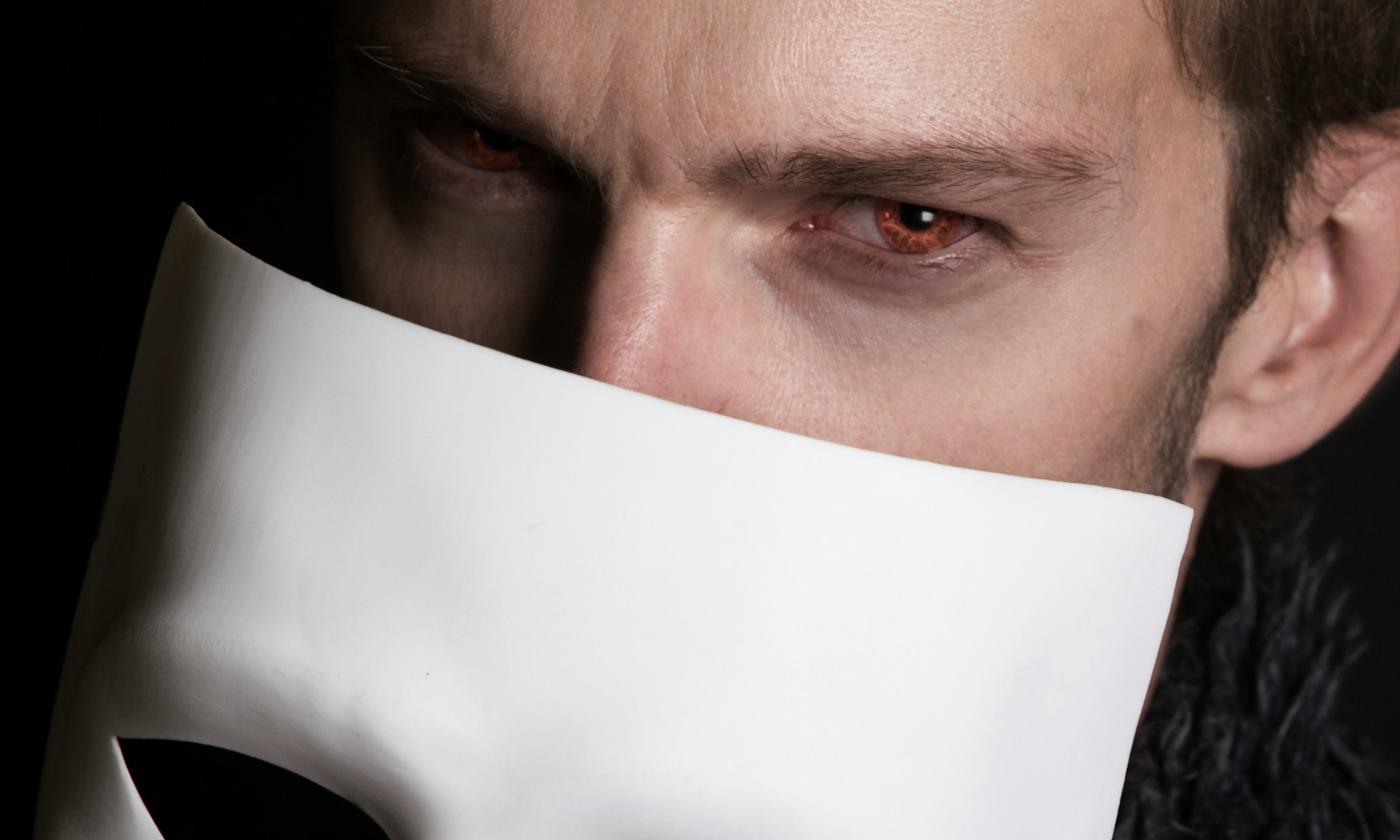 A vampire removes his mask, revealing his blood red eyes.