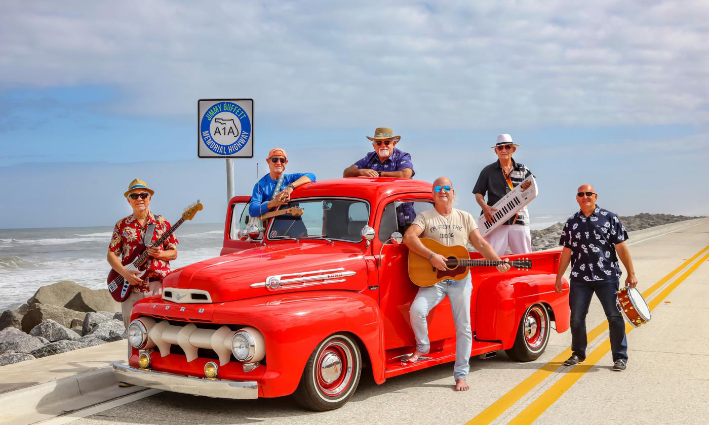 The band Landfall, with instruments, posed around and on an antique red truck near the water on A1A
