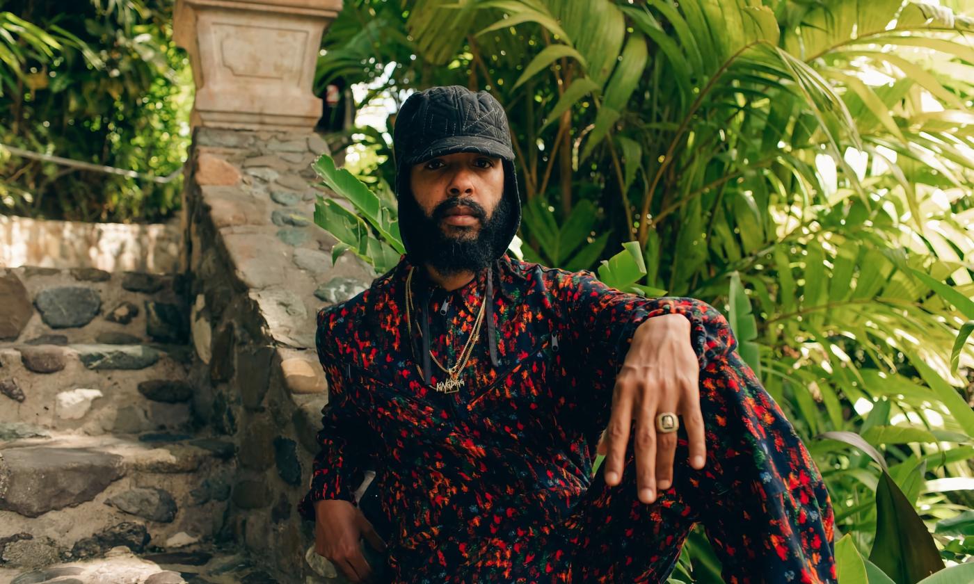 The raggae artist, Protoje, sitting on stone steps surrounded by palms