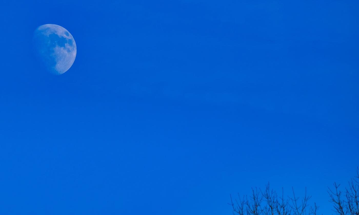 A nearly full moon in a dark blue sky