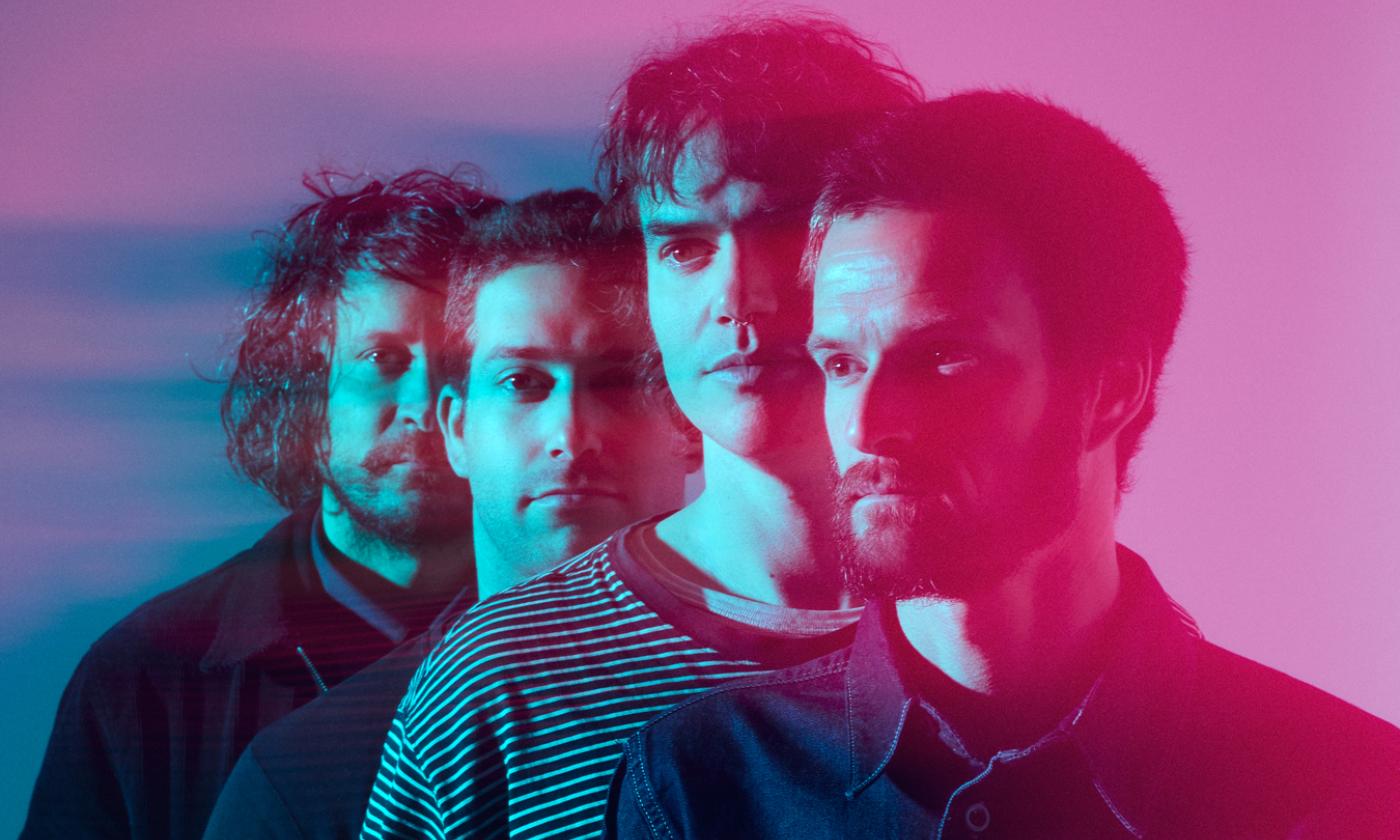 Bandmates from All Them Witches line up and pose in front of a pink and purple backdrop.