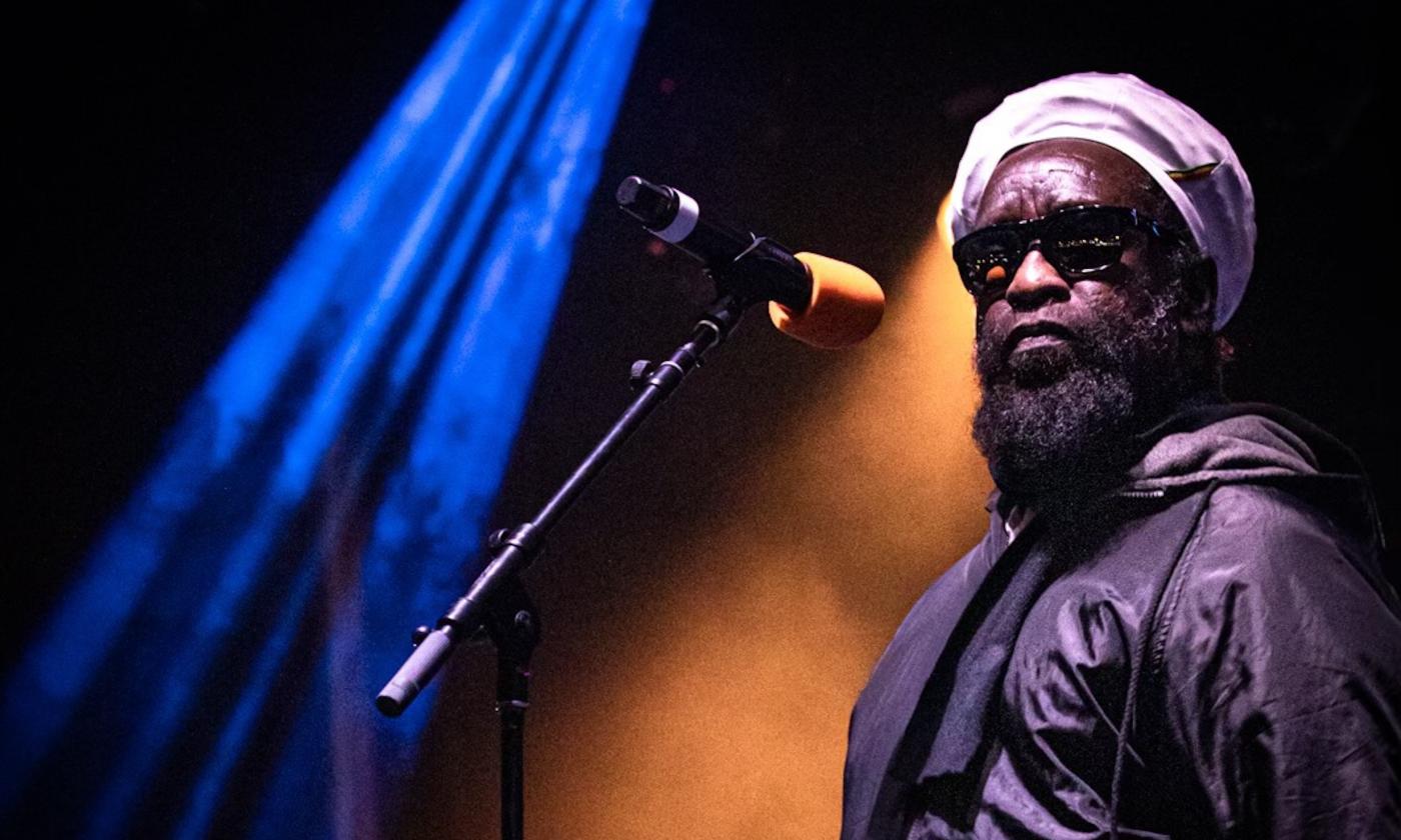 The lead vocalist from Black Uhuru poses on stage with black glasses. 