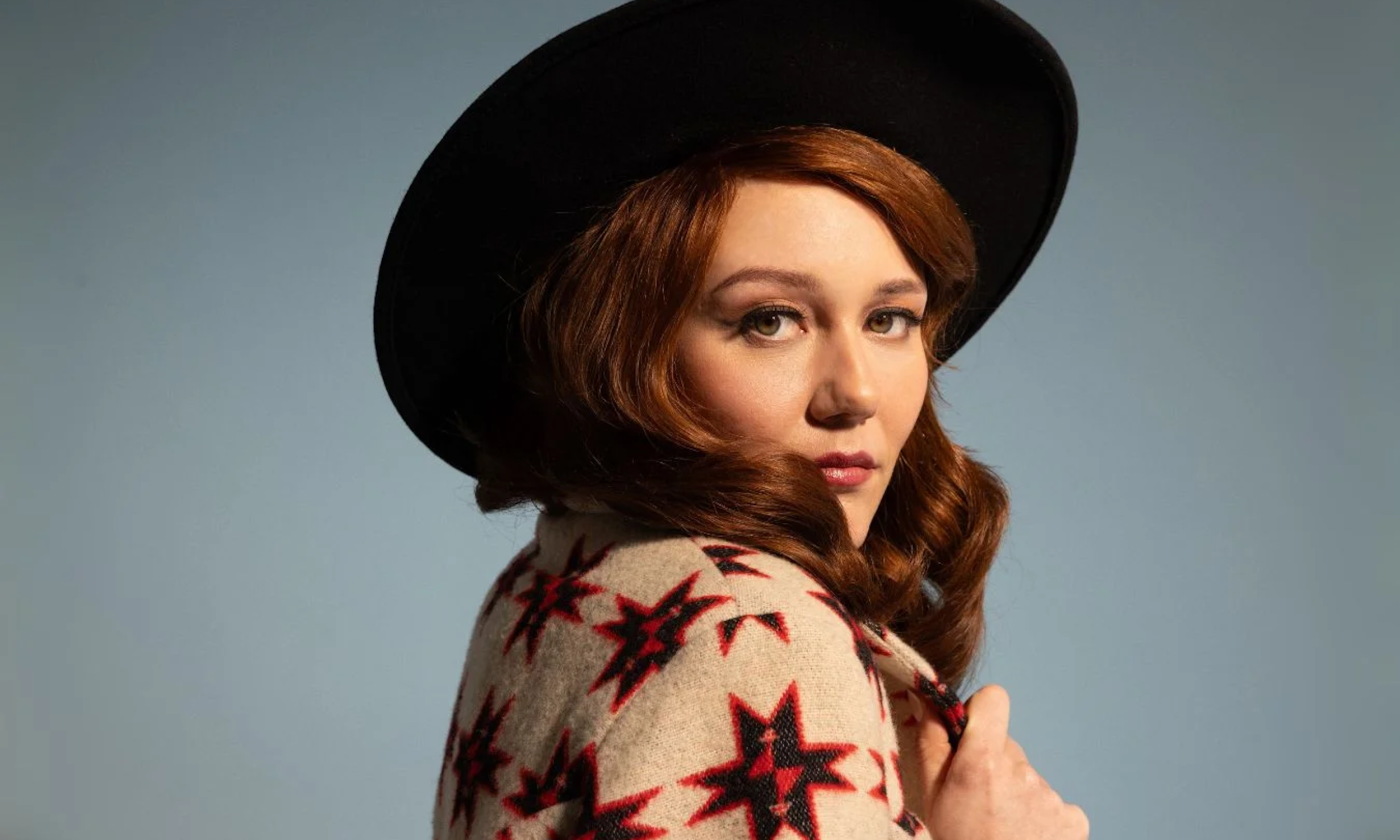 Mary Tuttle dons a black hat and poses in front of a blue backdrop.