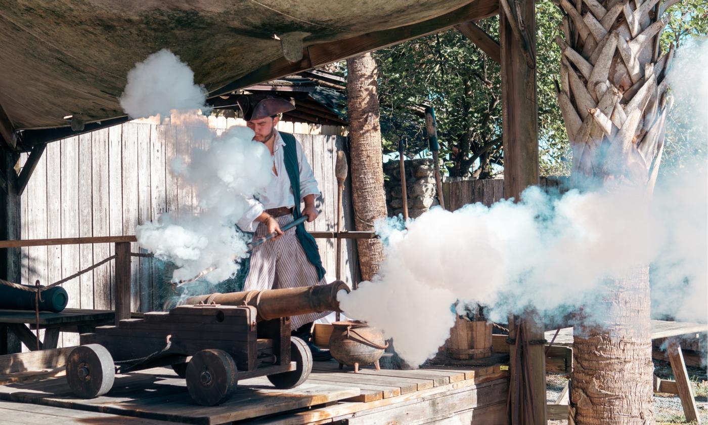 Man in colonial garb firing a small cannon