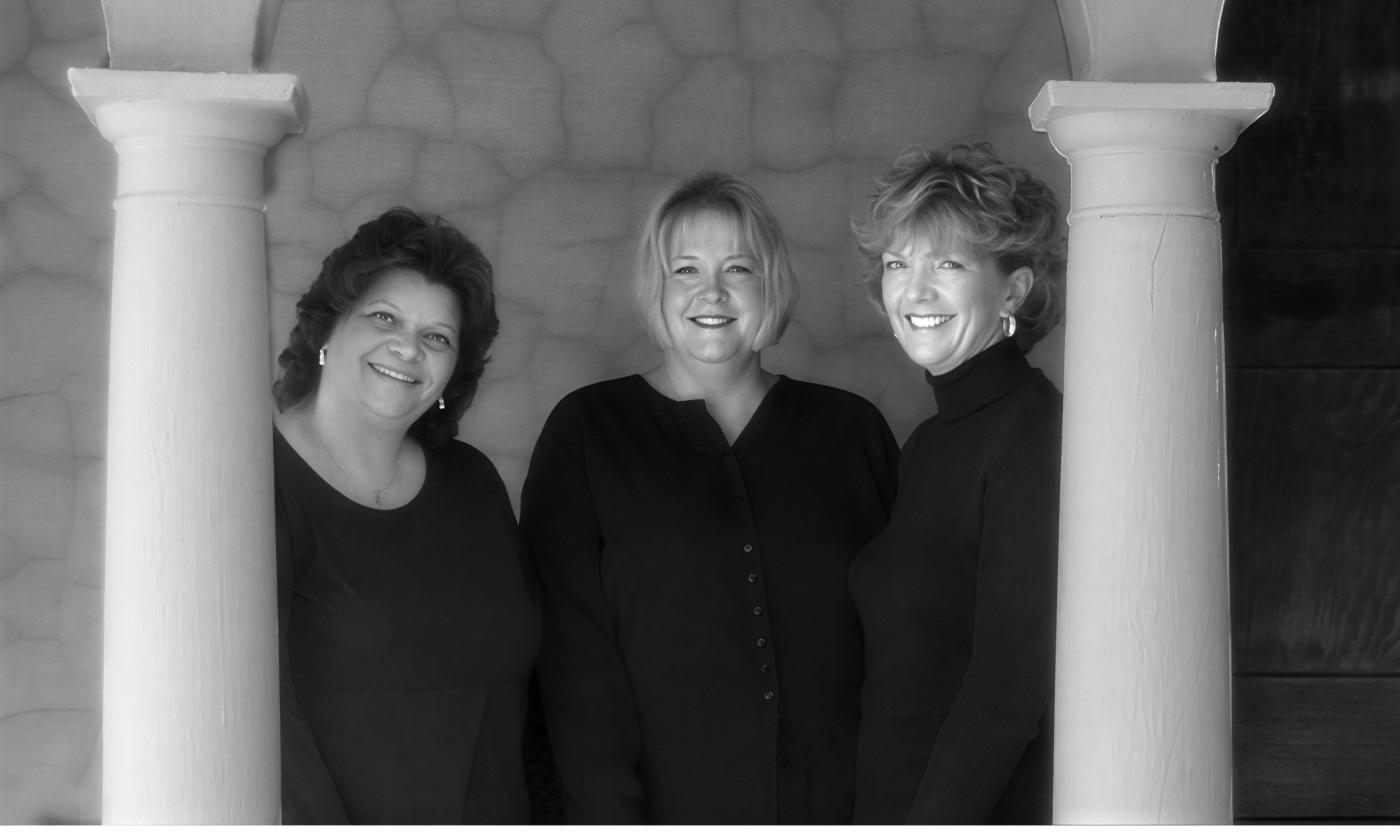 Three women in black, standing between white columns