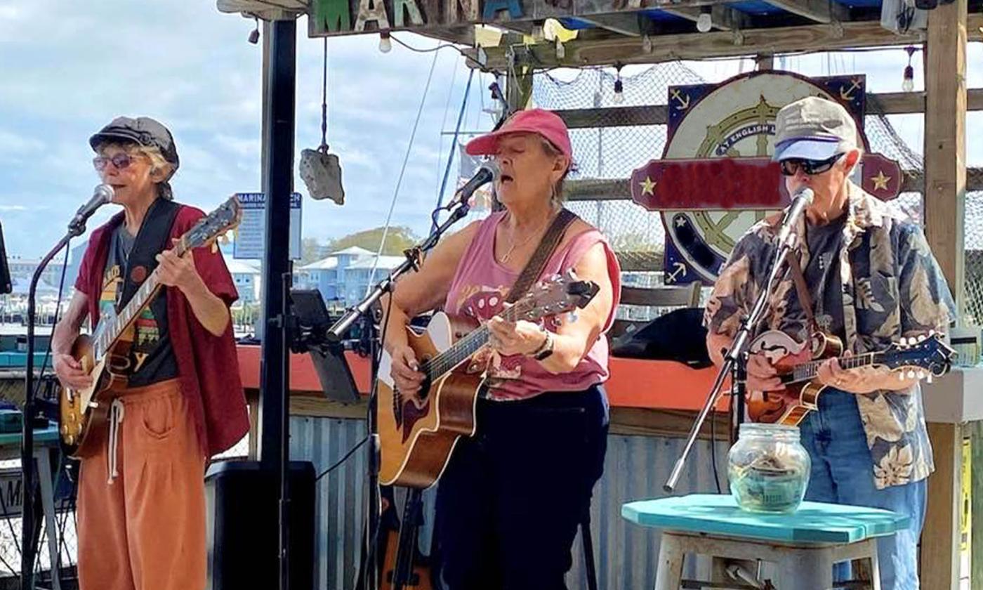 The band Honey Knots at a marina perfoming with guitars and mandolin.