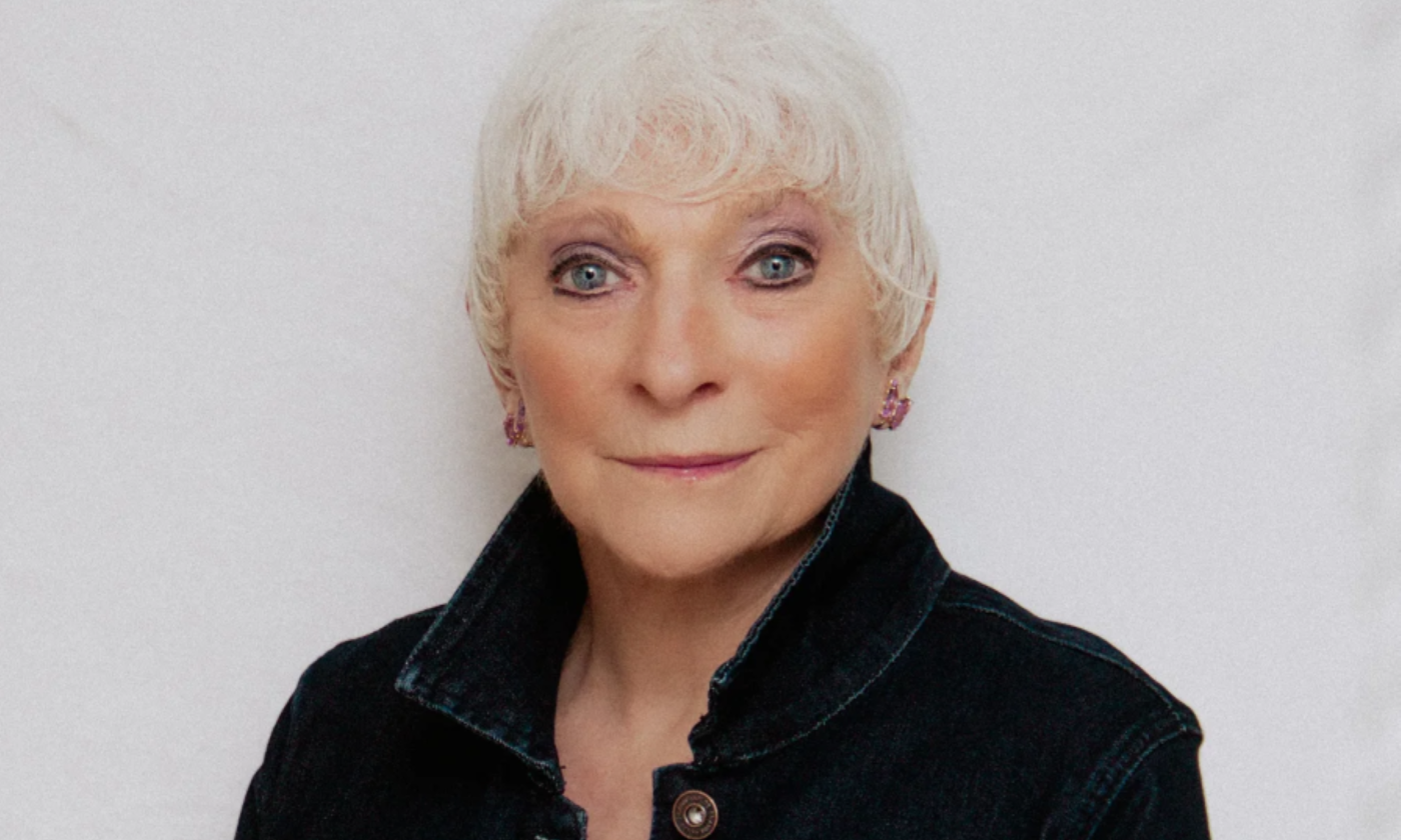 Judy Collins smiles and poses in front of a white backdrop.