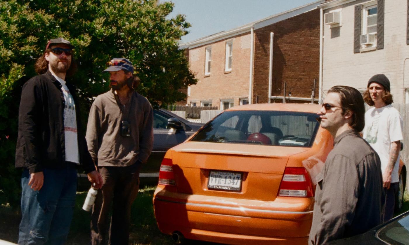 The four-member band Turnover, standing by an orange car used in their music video