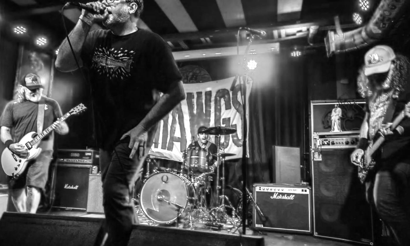 The five member band Hawgs, on stage depicted in a black and white photo