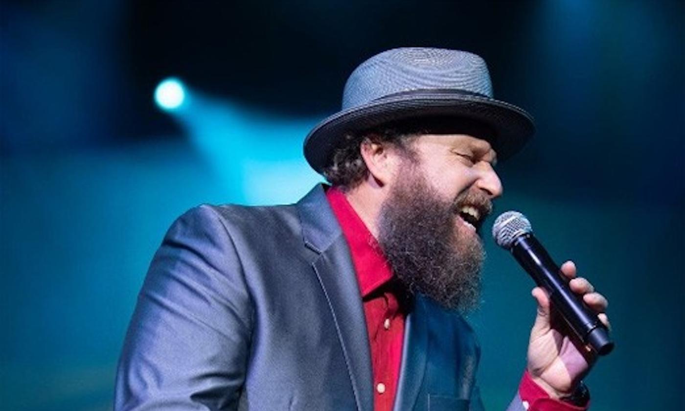 John Nemeth performs on stage in a blue blazer and a matching cap.