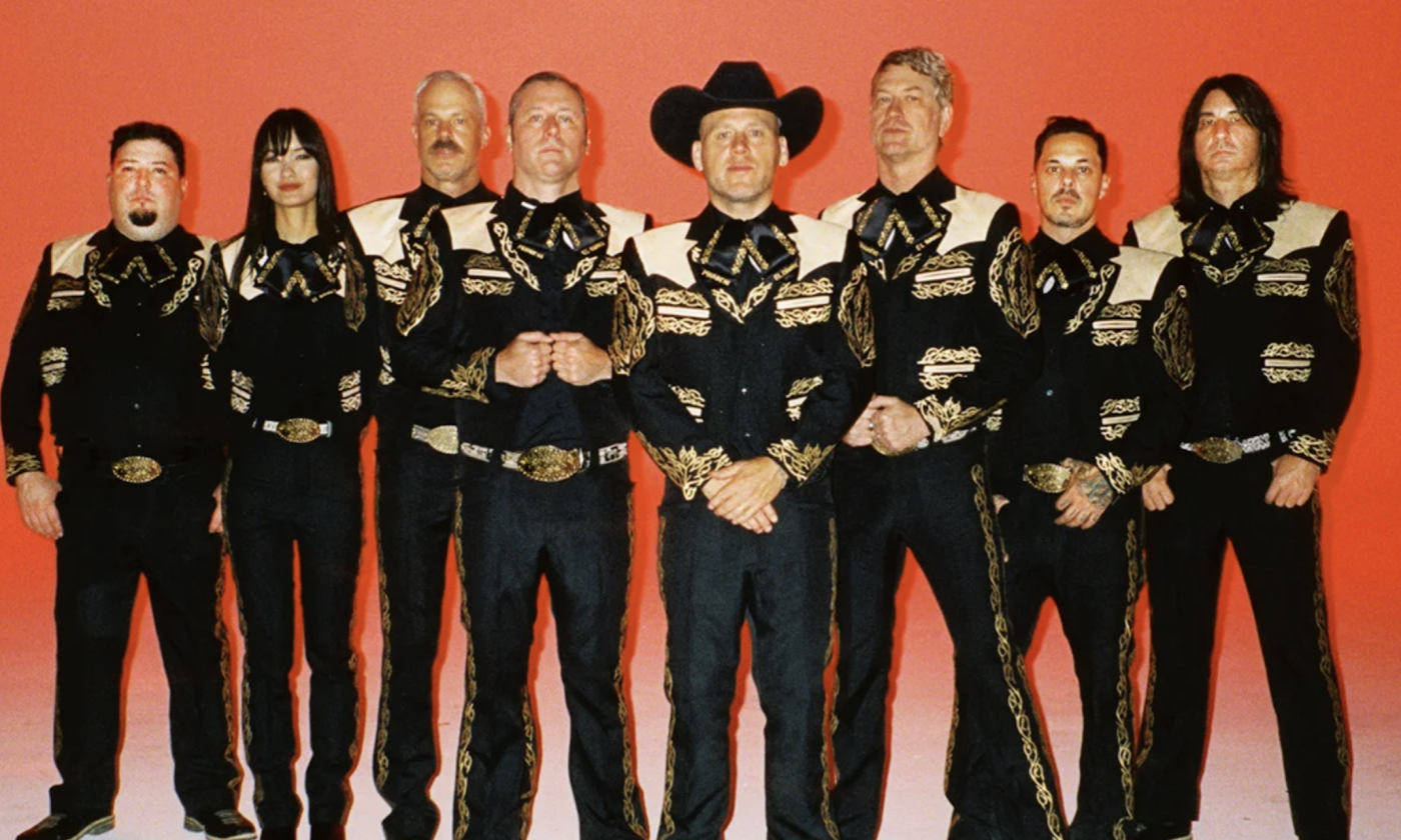 Bandmates from Mariachi El Bronx huddle together and pose in front of a red backdrop.