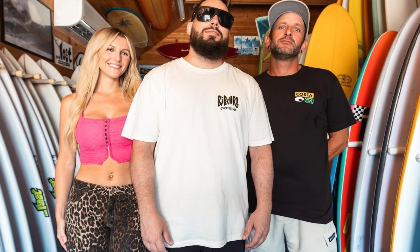 Bandmates from Seranation smile and pose next to surfboards.