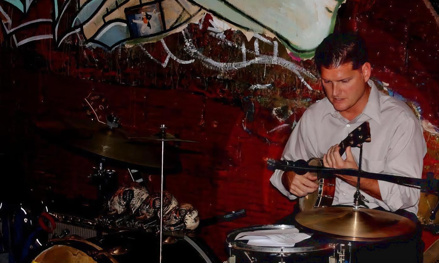 Darren Ronan playing the ukulele while sitting at the drums