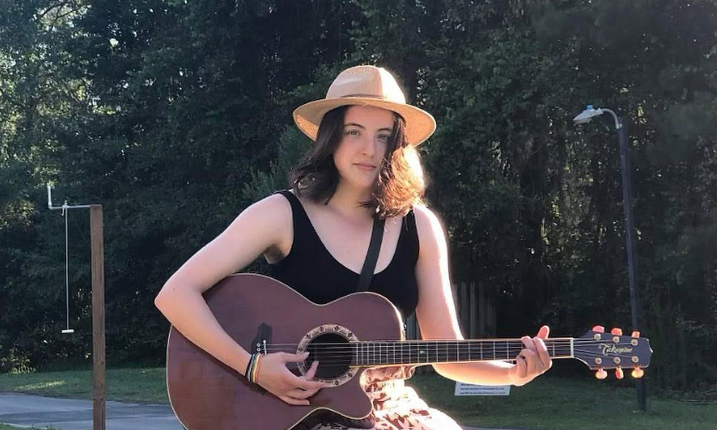 Songwriter Alivia Hunter, in a hat, with her guitar, outsite