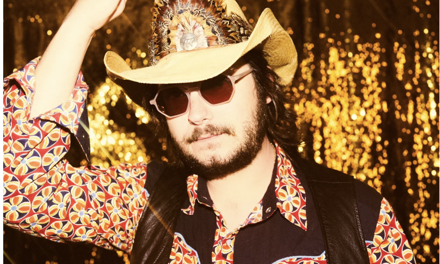 Eddie 9V poses with a cowboy hat, glasses, and a printed shirt with vest.
