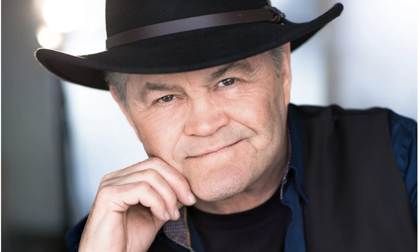 Micky Dolenz wears a black hat with matching blazer and poses for fans. 