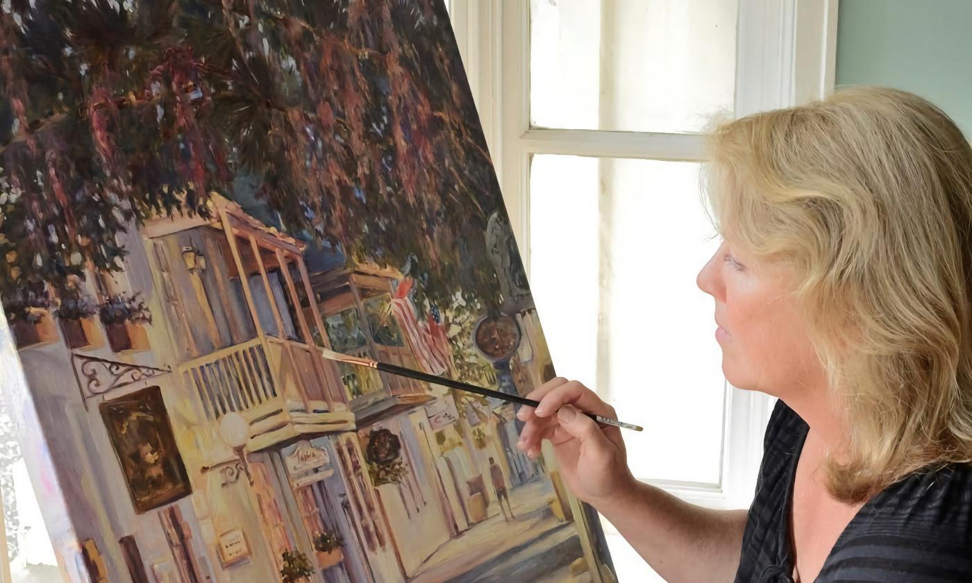 Artist Marther Ferguson, sitting an an easel and painting an outdoor scene