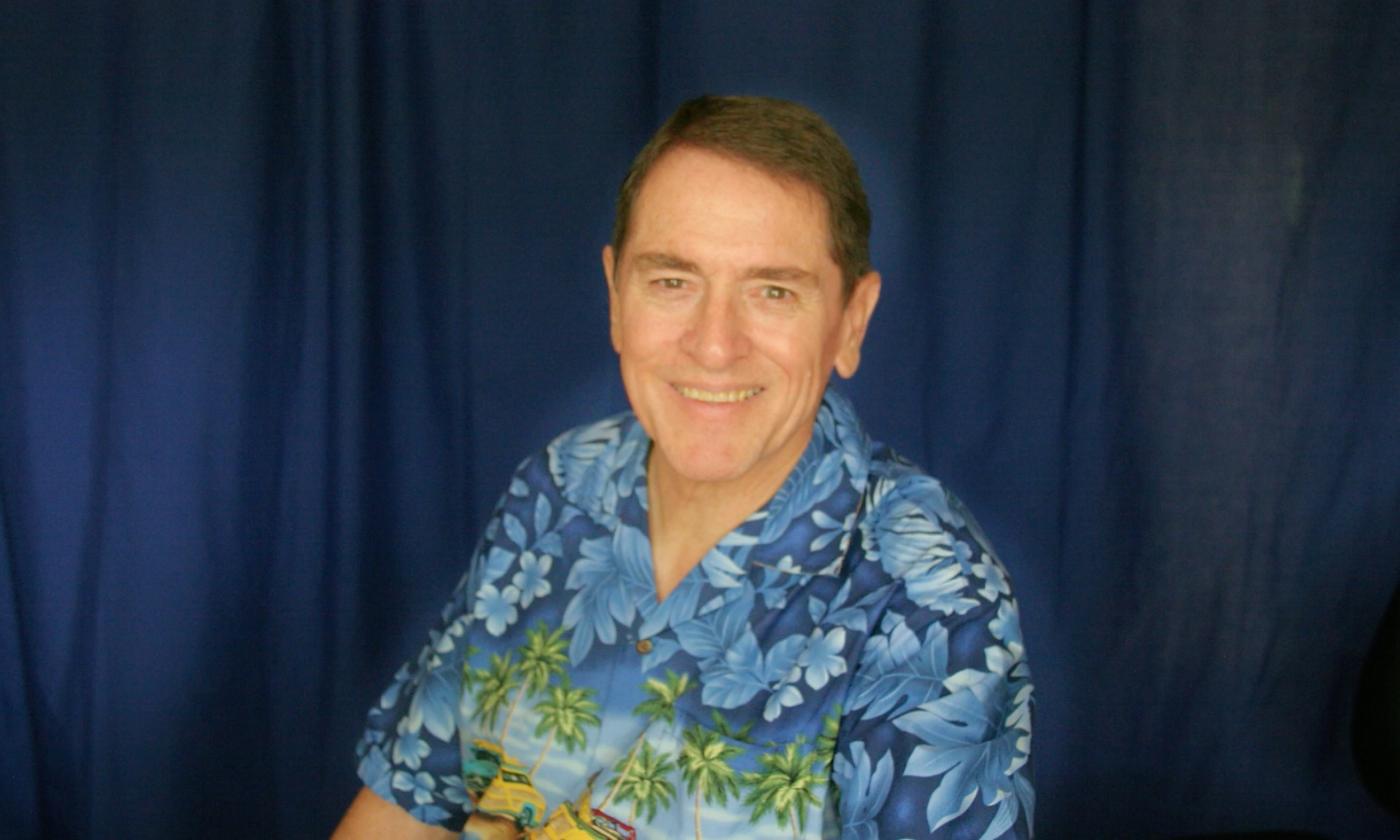 Michael Doyle, singer, wearing a blue tropical shirt and sitting in front of a blue curtain