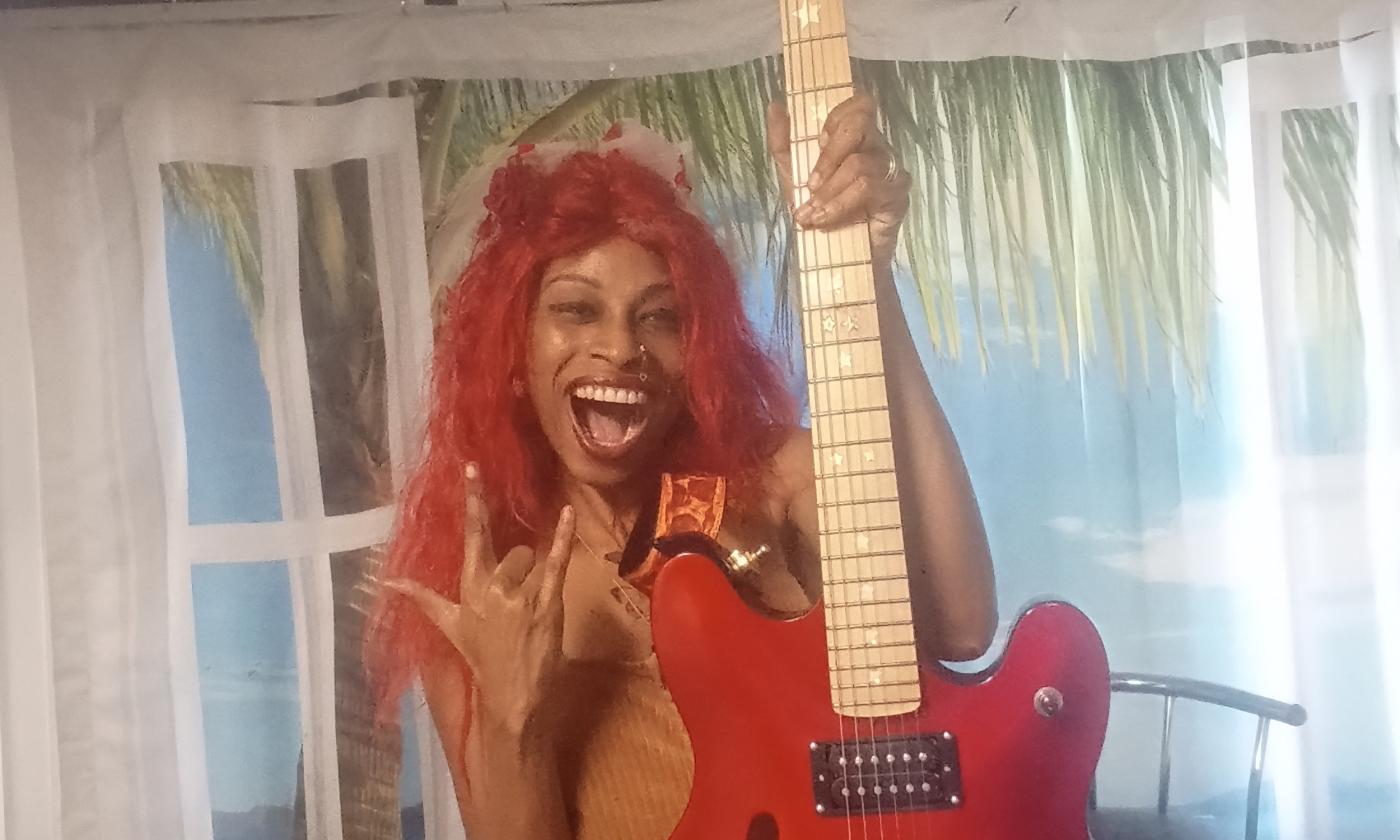 Lydia Flowers against a curtained wall, holding an electric guitar
