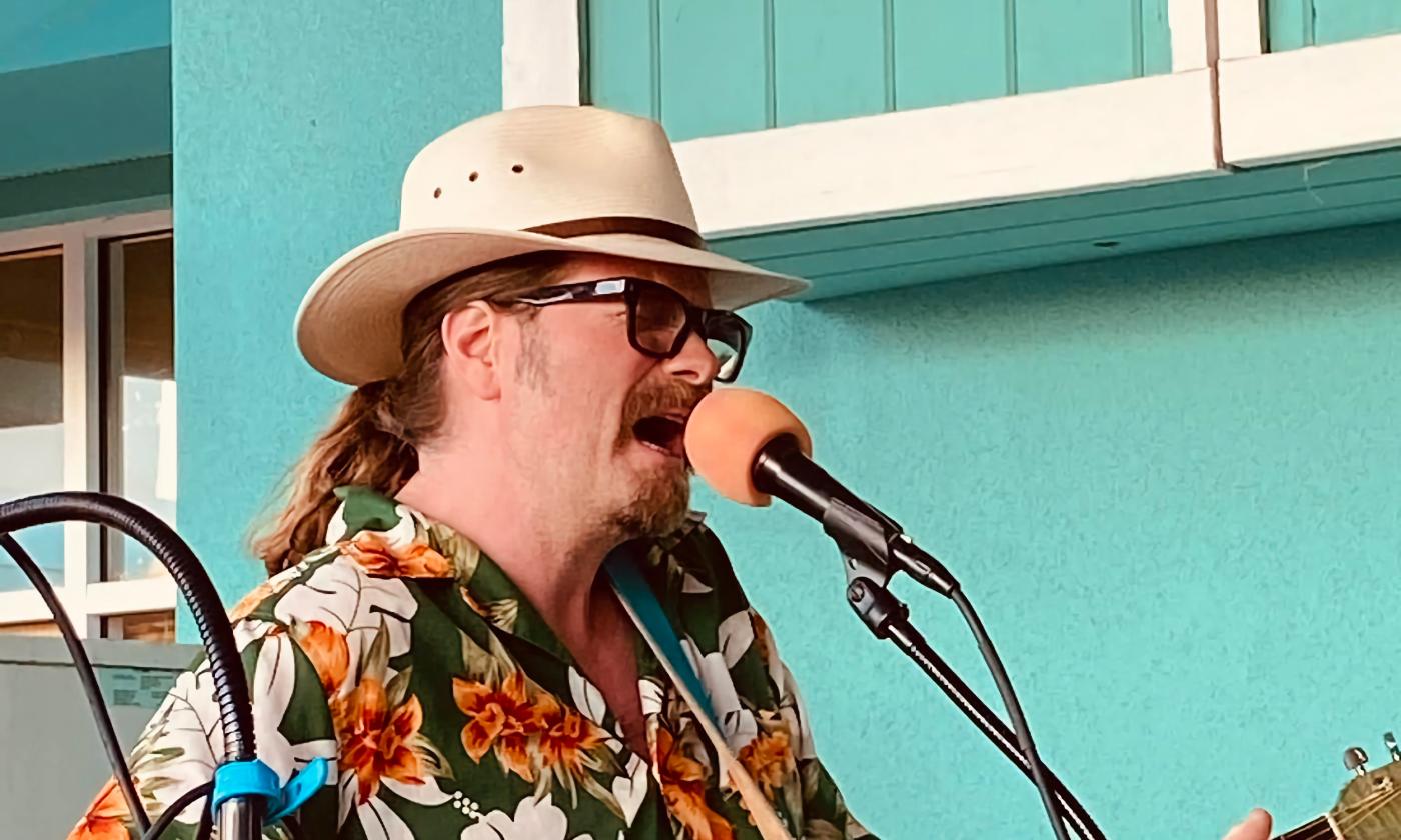 Michael P. Owen performing outside a bright teal building