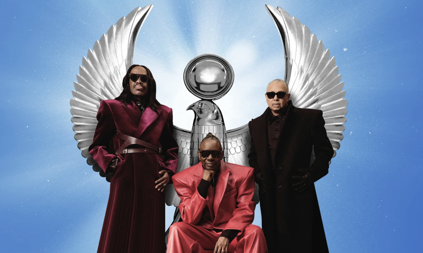 Earth, Wind, and Fire smile and pose in front of a blue backdrop.