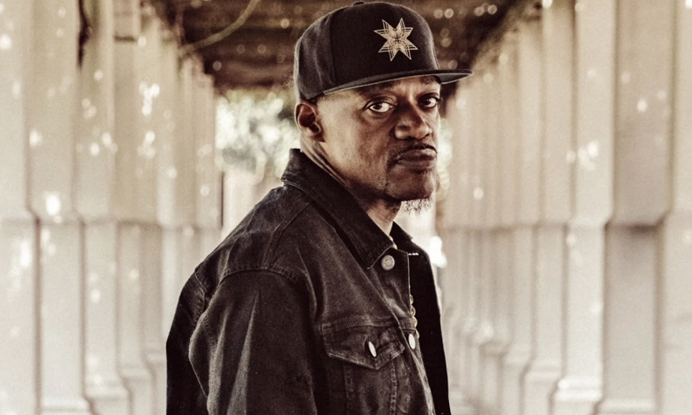 Eric Gales dons urban denim clothing and poses in front of a blurred backdrop.