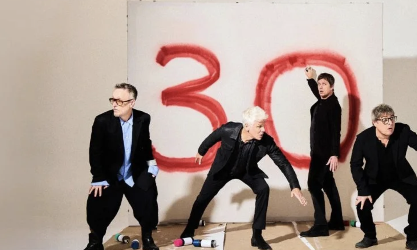 Bandmates from Matchbox 20 don black clothing and pose in front of a white wall. 