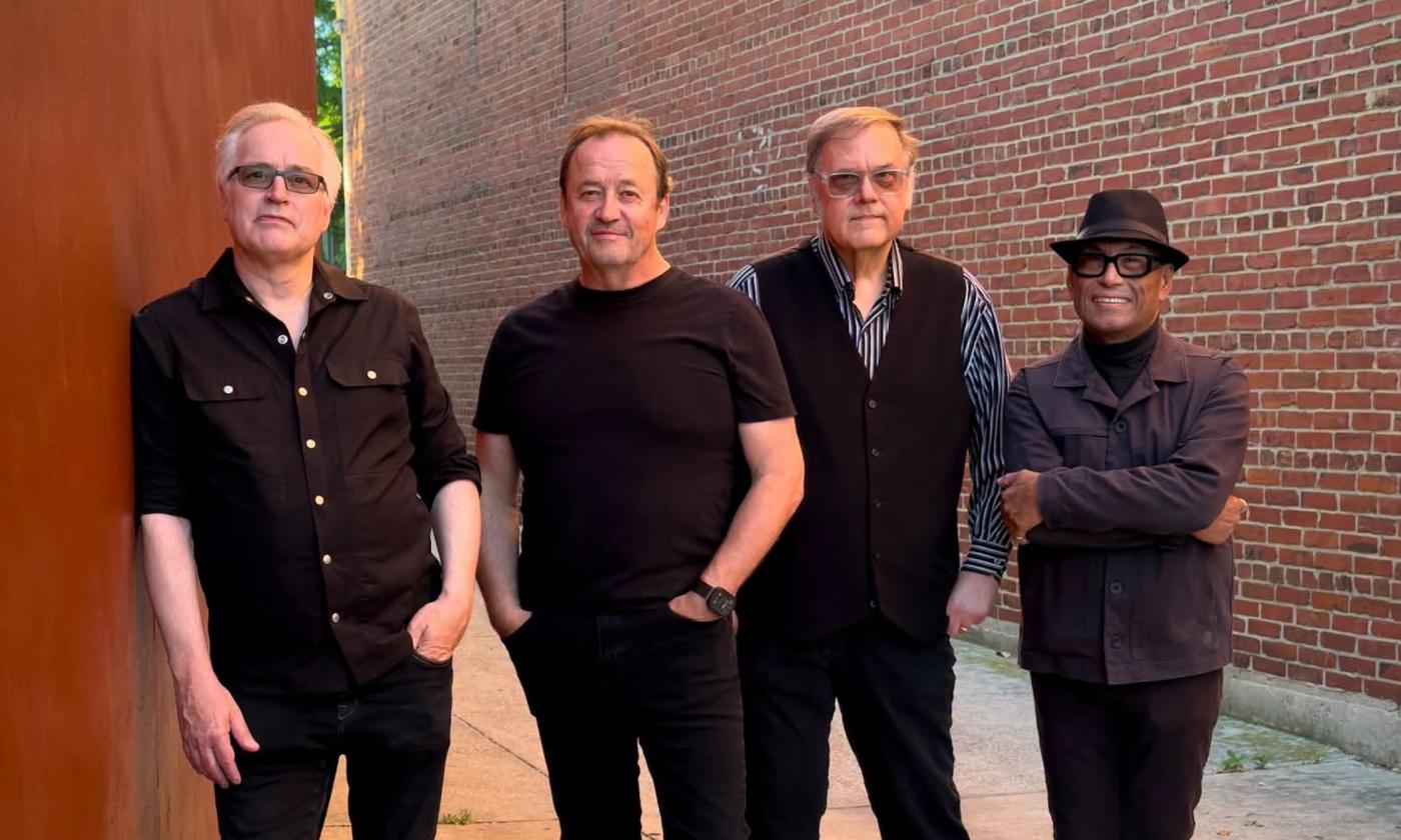 Bandmates from The Smithereens pose with a brick wall as their backdrop.