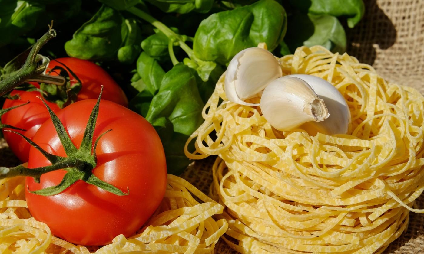 A red, green and white display of fresh foods, tomato, basil, garlic, and pasta 