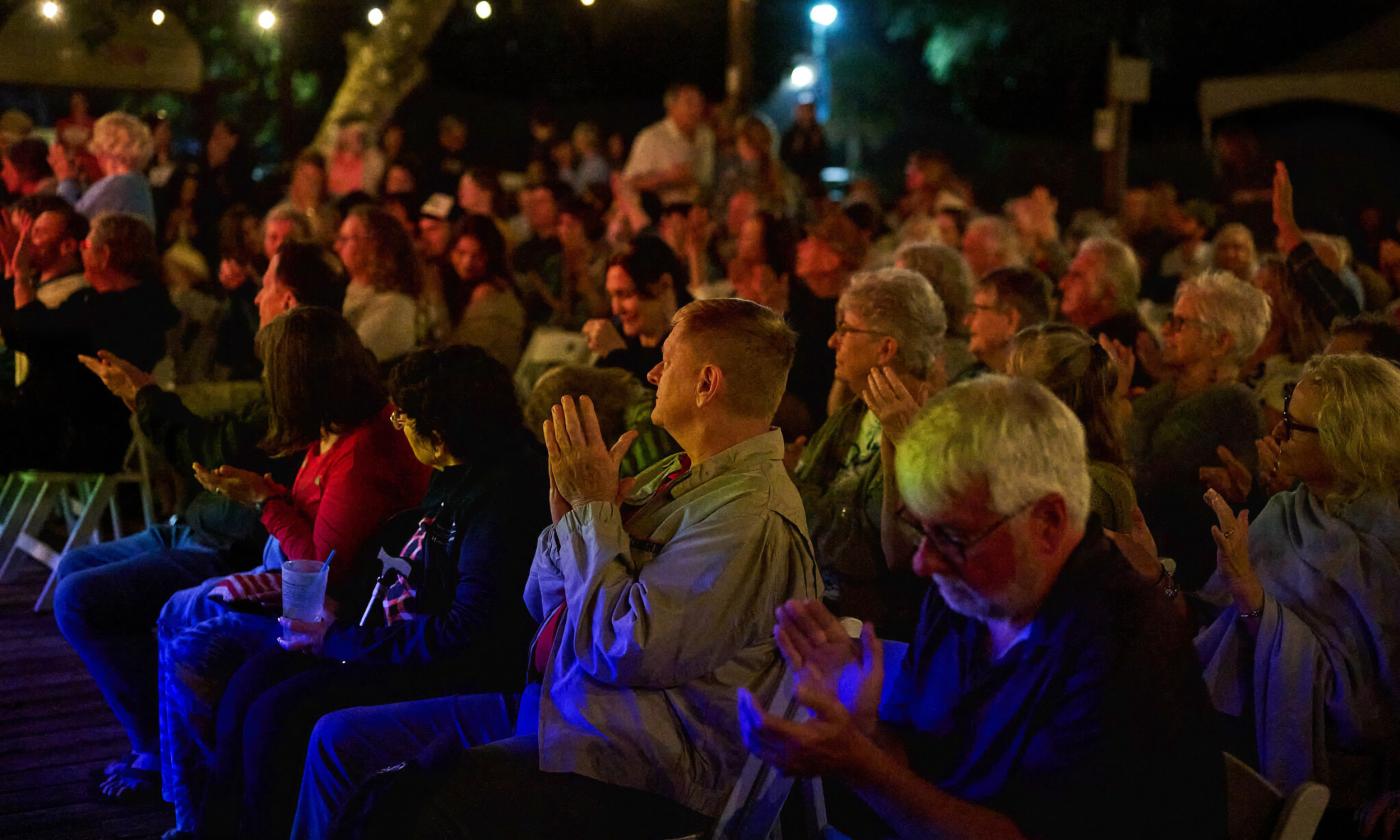 The audience at an outdoor event applauding after a speaker