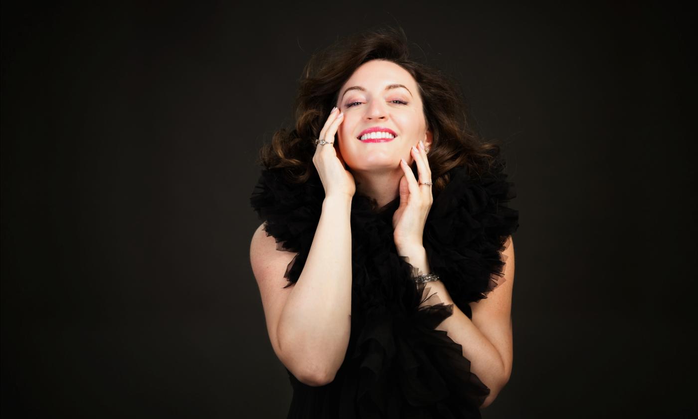 Susanna Barasch in black, with a feather boa against a black background