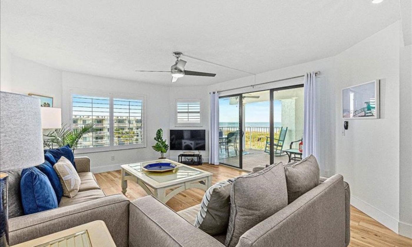 The living room of a vacation rental condo with matching grey furniture and a balcony seen through a sliding glass door. 